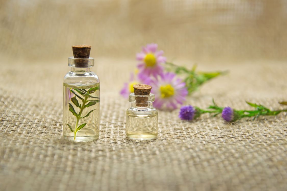Glass bottles of essential oil with fresh flowers on burlap — aromatherapy oils and tinctures